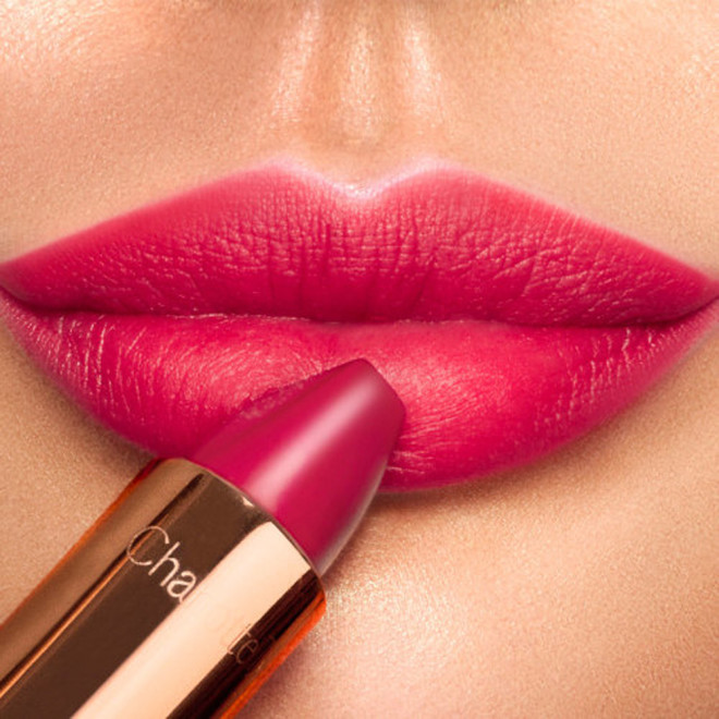 Lips close-up of a light-tone model applying lipstick in a vivid pink shade with a matte finish.