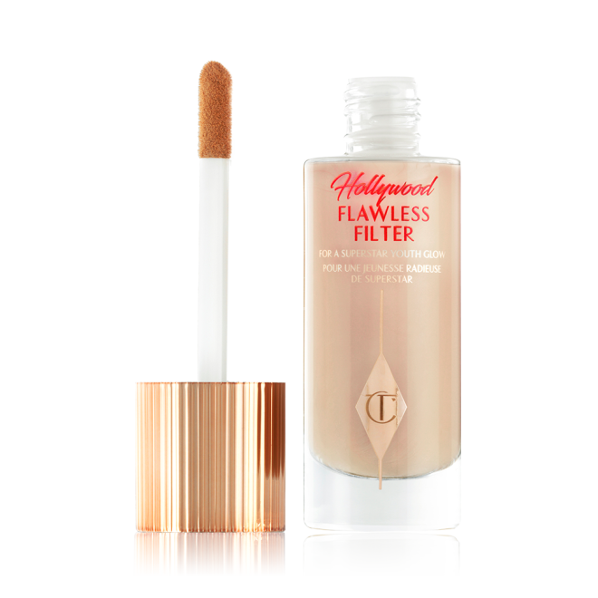 An open, luminous primer in a light cool-toned-beige shade in a glass bottle with its gold and white doe-foot applicator next to it.