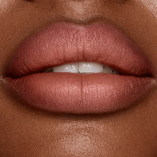 Matte Revolution Lipstick in Supermodel deep lips close-up Lips closeup of a deep-tone model applying a mid-toned muted nude-rose matte lipstick.