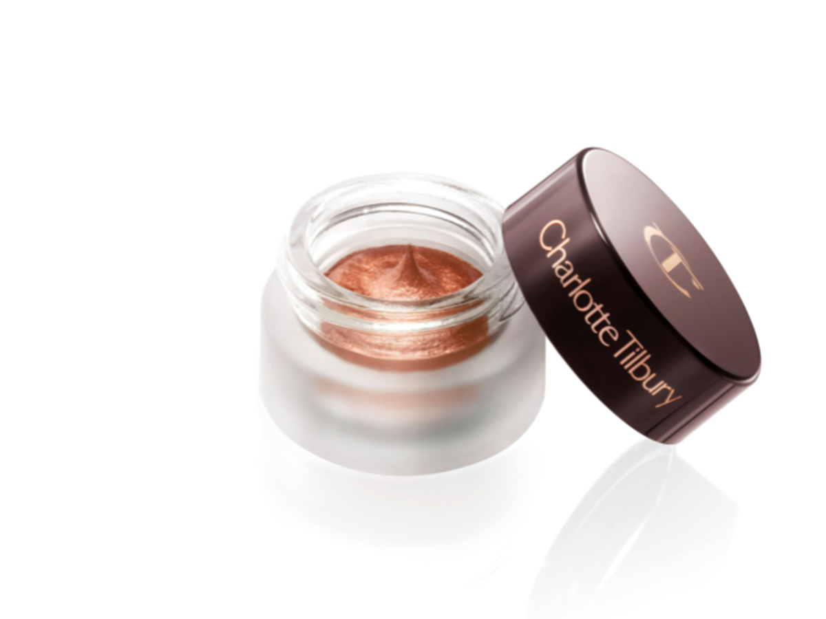 An open glass pot with shimmery russet rose cream eyeshadow with golden-peach sparkle and its lid placed next to it.