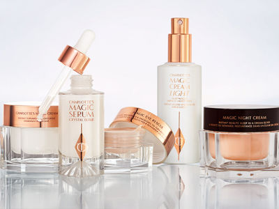 Pearly-white face cream in a glass jar with a gold-coloured lid, luminous ivory-coloured serum in a glass bottle with a white and gold-coloured dropper lid, fawn-coloured eye cream in a petite glass jar, face cream in a white-coloured bottle with a gold-coloured pump, and peach-coloured face cream in a glass jar with a dark brown and gold-coloured lid.