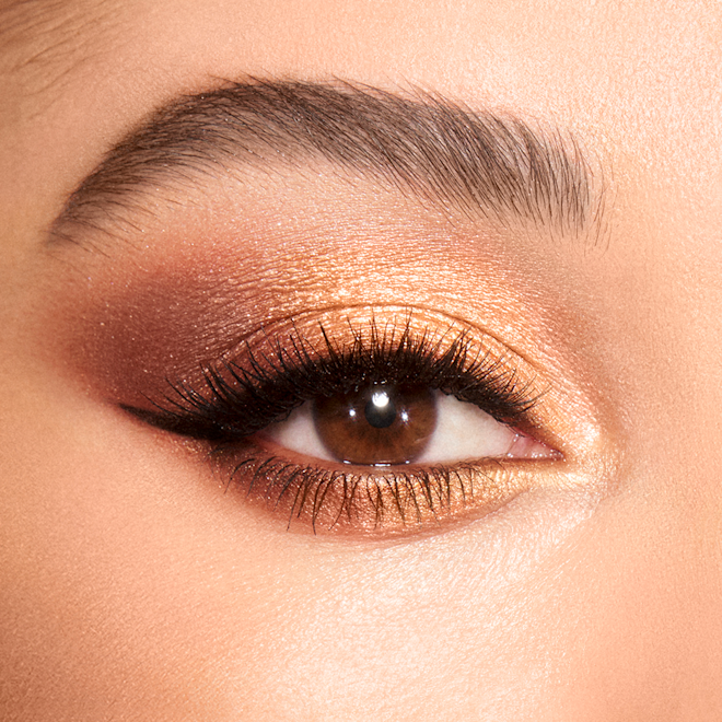 Luxury Palette in Queen of Glow eye look on brown eyes close-up Close-up of a light-tone model's brown eyes with shimmery brown, gold, and champagne eye makeup.