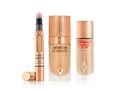 Glowy primer in a glass bottle with a gold-coloured lid, foundation in a frosted glass bottle with a gold-coloured lid, and an open, golden-coloured tube of liquid concealer with a soft, sponge applicator at the end.