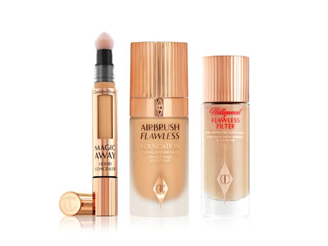 Glowy primer in a glass bottle with a gold-coloured lid, foundation in a frosted glass bottle with a gold-coloured lid, and an open, golden-coloured tube of liquid concealer with a soft, sponge applicator at the end.