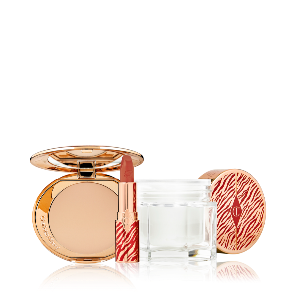 An open pressed powder compact with a mirrored lid with an open lipstick tube in a vivid red shade in a gold-coloured tube with red tiger stripes on it, and an open glass jar of pearly-white cream with its gold-coloured lid with red tiger stripes on it for the Lunar New Year. 