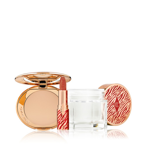An open pressed powder compact with a mirrored lid with an open lipstick tube in a vivid red shade in a gold-coloured tube with red tiger stripes on it, and an open glass jar of pearly-white cream with its gold-coloured lid with red tiger stripes on it for the Lunar New Year. 