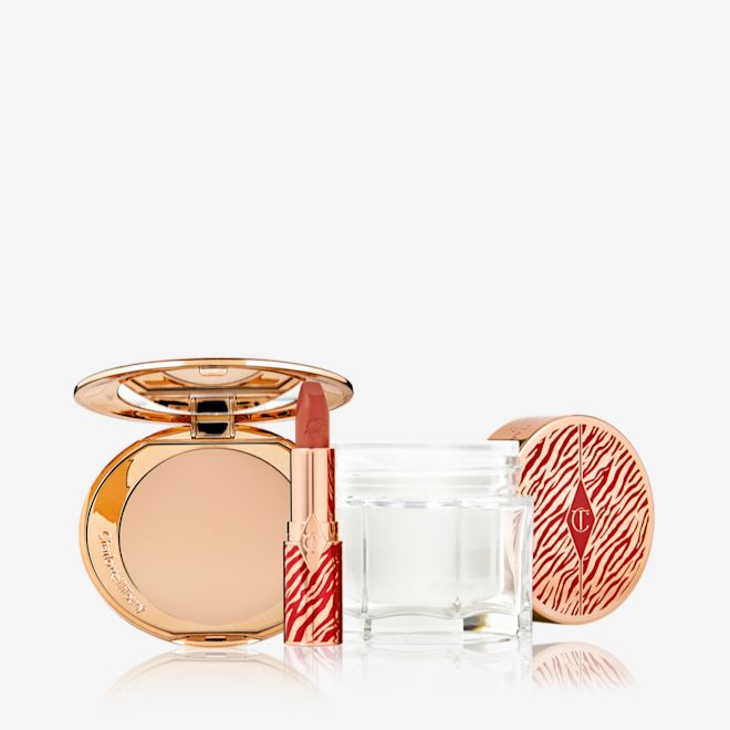 Lunar New Year Beauty Secrets kit open An open pressed powder compact with a mirrored lid with an open lipstick tube in a vivid red shade in a gold-coloured tube with red tiger stripes on it, and an open glass jar of pearly-white cream with its gold-coloured lid with red tiger stripes on it for the Lunar New Year.