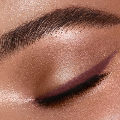 Single-eye close-up of a deep-tone model wearing a dark berry-brown eyeliner in a wing style.