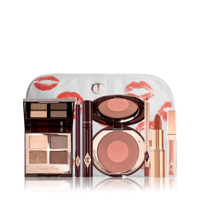 An open, mirrored-lid eyeshadow palette in matte and shimmery gold, brown, and beige shades, an open black eyeliner pencil, a mascara in a dark-crimson colour scheme, a burnt orange lipstick with a matching lip liner pencil, nude-peach lip gloss, and an open two-tone blush in medium brown-pink. 