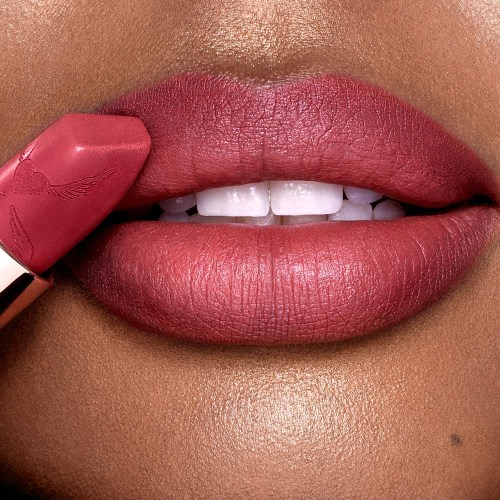 Lips close-up of a deep-tone model applying a matte berry-rose lipstick. 