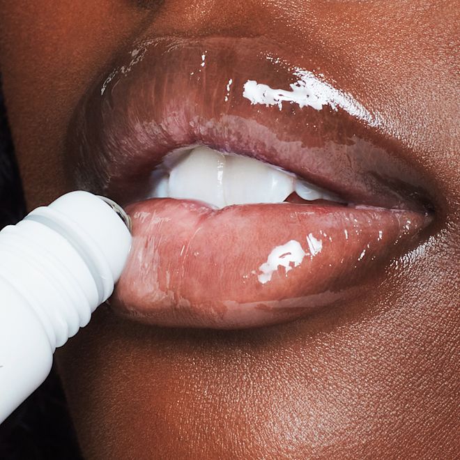 Charlotte's Magic Lip Duo on deep-tone lips close-up lips close-up of a deep-tone model applying a lip oil on her lips after exfoliating with a lip scrub.