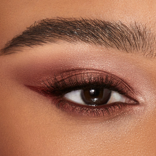Single-eye close-up of a deep-tone model with brown eyes wearing a shimmery russet rose cream eyeshadow with a golden sparkle. 