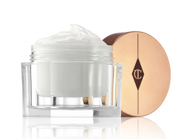 Close-up of a thick, pearly-white face cream in a glass jar with a golden-coloured lid. 