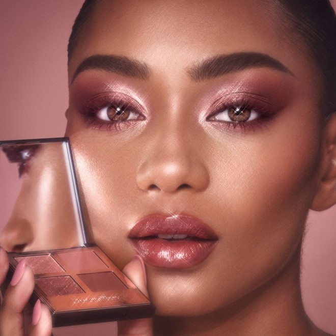 Deep-tone model with hazel eyes wearing berry pink lipstick with a gloss on top with eye makeup in shades of pearlescent rose gold, dusky rose, berry brown and rose-bud pink,