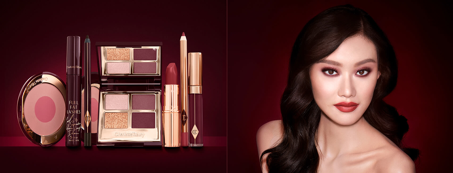 A fair-tone model with brown eyes wearing reddish-plum eye makeup, glowy face base, and a vampy-red lipstick with a satin-finish, along with an open, mirrored-lid eyeshadow palette in matte and shimmery gold and red shades, an open black eyeliner pencil, a mascara in a dark-crimson colour scheme, a red lipstick with a matching lip liner pencil, vampy-red lip gloss, and an open two-tone blush in cool pink. 