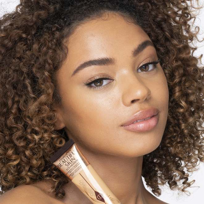 Medium-dark-tone brunette model wearing glowy, skin-like foundation with a fresh, satin finish with a nude lipstick, and subtle eye makeup.