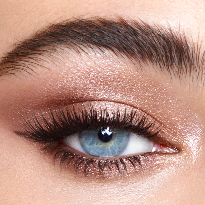 Single-eye close-up of a fair-tone model with blue eyes wearing shimmery champagne, metallic pink, and smokey brown eye makeup.