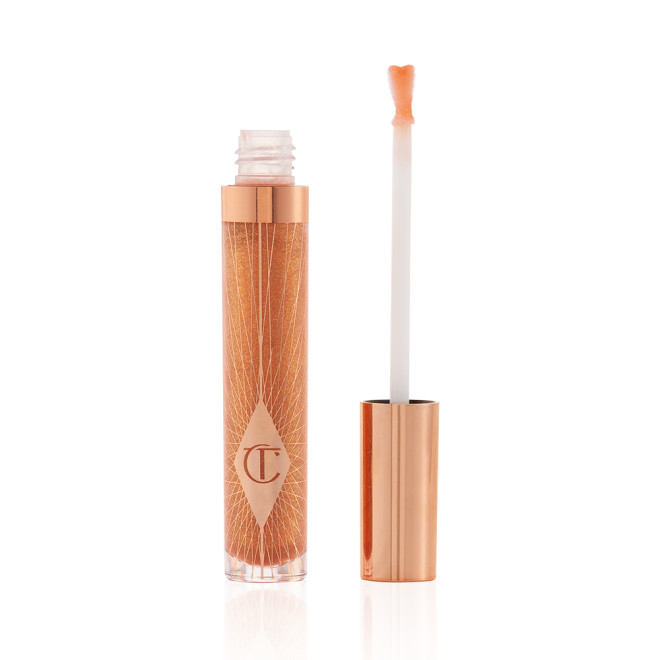 A lip gloss in a sheer gold shade in a glass tube with its heart-shaped applicator next to it.