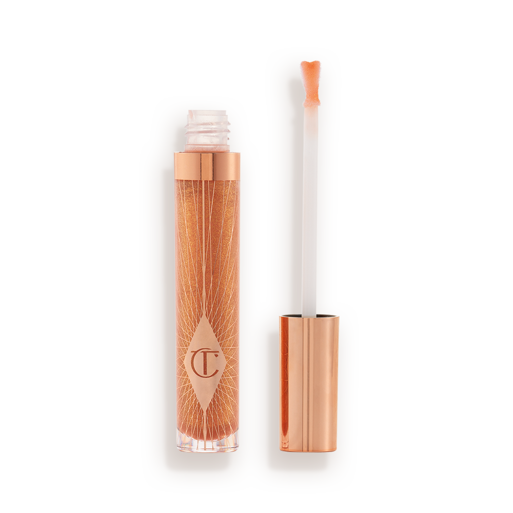 A lip gloss in a sheer gold shade in a glass tube with its heart-shaped applicator next to it.