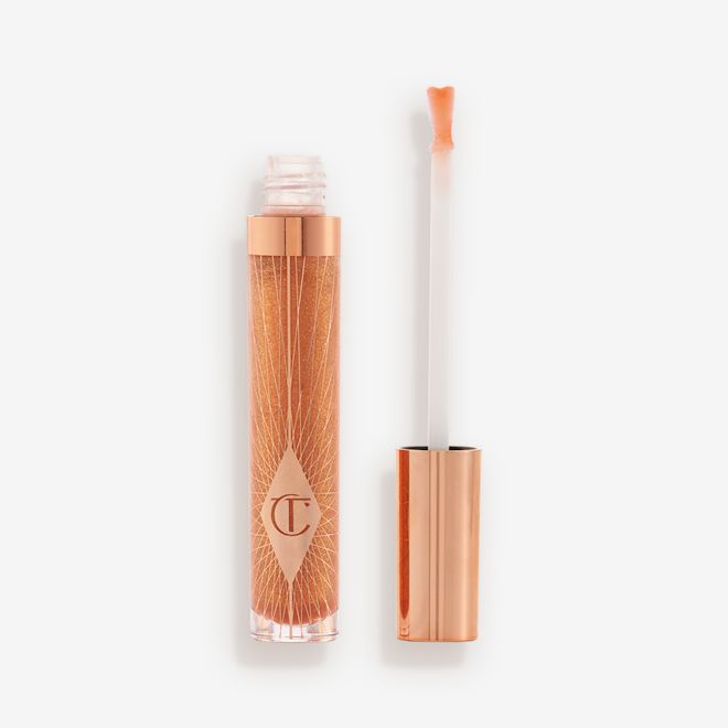 Collagen Lip Bath in Gold lid removed A lip gloss in a sheer gold shade in a glass tube with its heart-shaped applicator next to it.