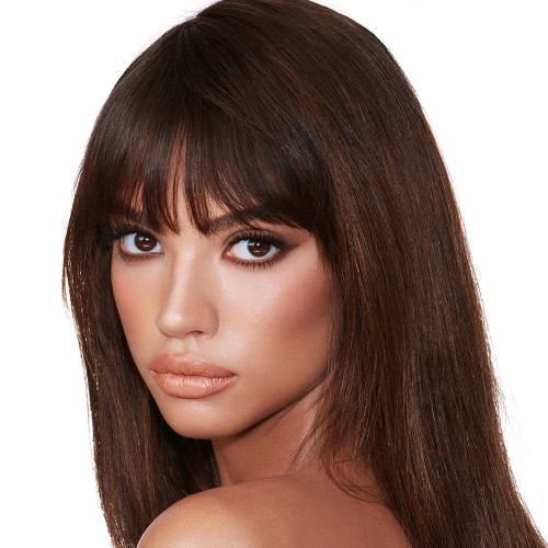 A medium-tone model with brown eyes wearing smokey brown eye makeup with muted pink blush with glossy soft-brown lips