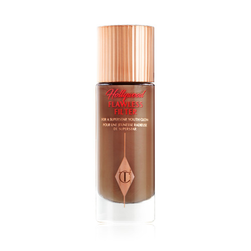 A closed, luminous primer in a dark brown shade in a glass bottle with a gold-coloured lid.
