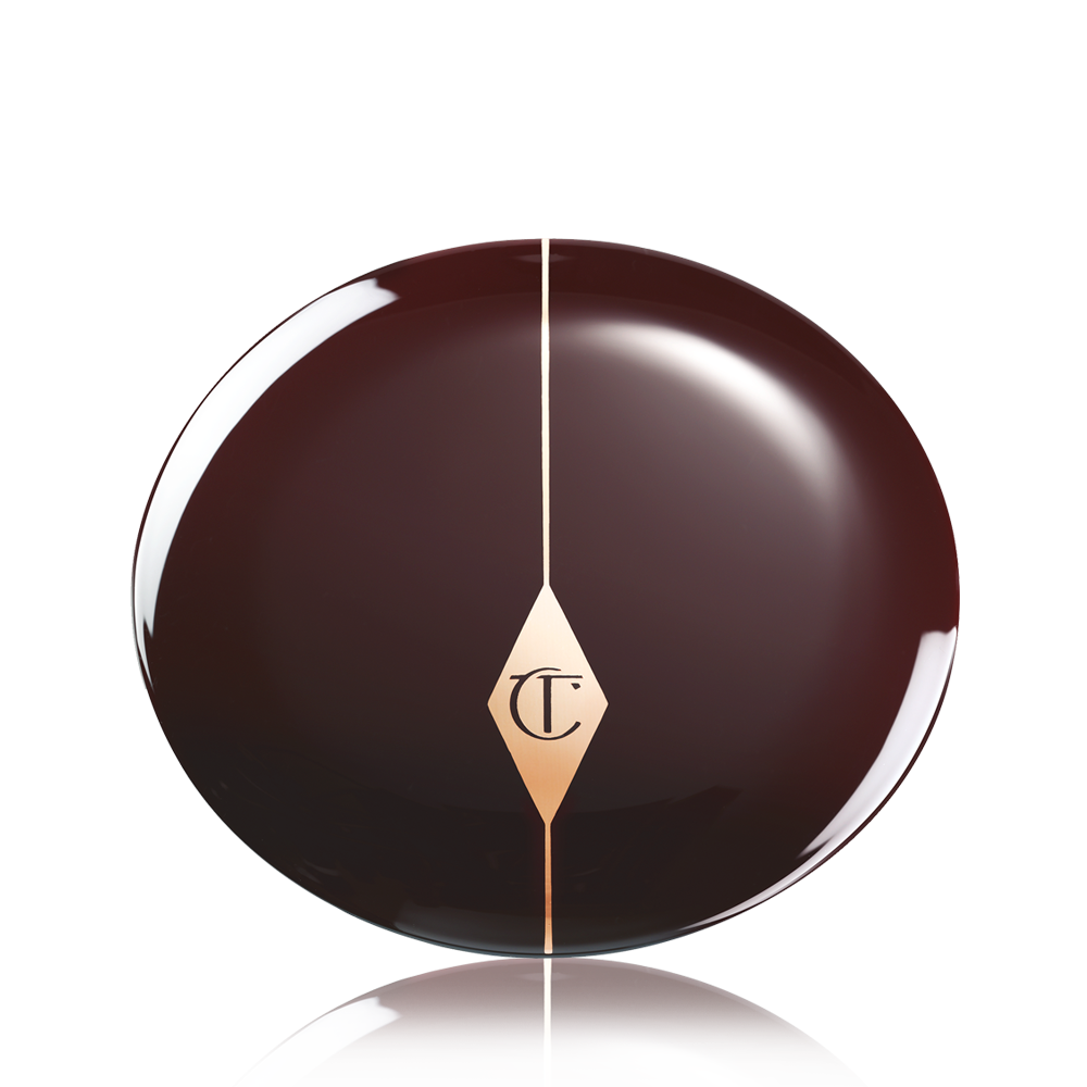 A closed blush compact in a dark crimson shade with the CT logo printed in the middle in a gold shade,