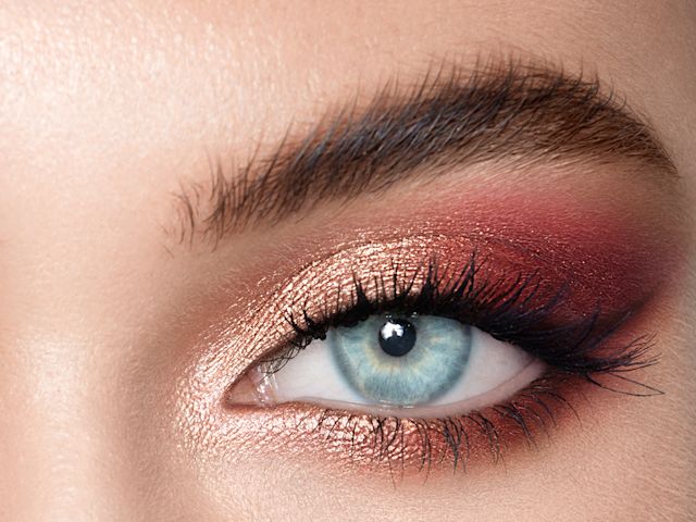 Close-up of a light-tone model's blue eye with shimmery rose gold and red eye makeup. 
