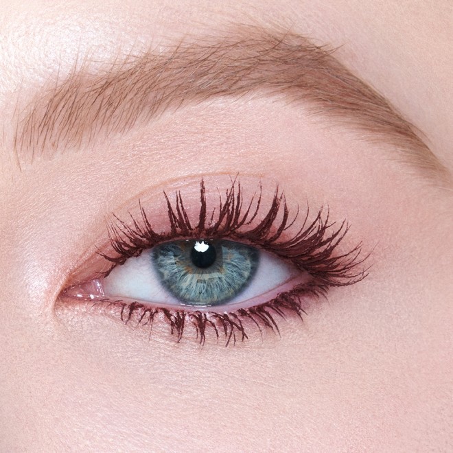 Single-eye close-up of a fair-tone model with blue eyes wearing a berry-brown, lengthening mascara that gives her lashes the appearance of false lashes.