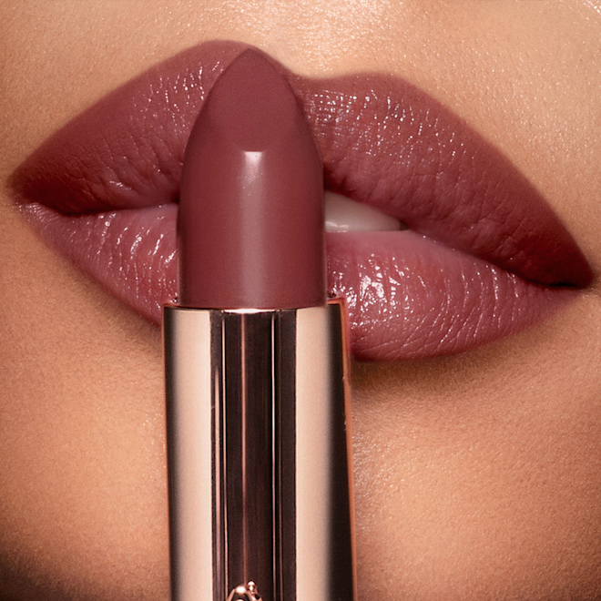 K.I.S.S.I.N.G Pillow Talk Intense Lipstick olive skin model A deep, berry-pink lipstick in a metallic, golden tube held up in front of an olive skin model wearing the same shade.