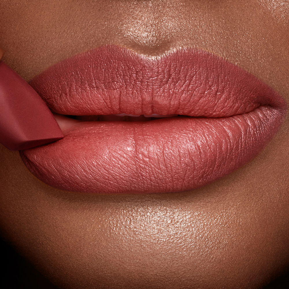 Lips close-up of a deep-tone model wearing a matte lipstick in a soft, muted berry-rose colour. 
