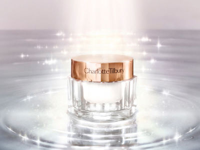A face moisturizer in a glass jar with a rose gold metallic lid on top of glimmering water. 