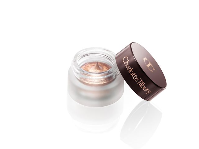An open, cream eyeshadow in a shimmery, soft champagne shade in a glass pot with its lid next to it. 