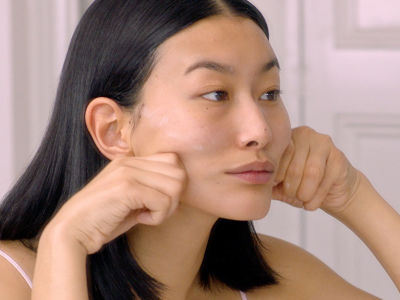 Close-up of a lights-skin model squeezing a skincare product on her fresh, make-up-free face. 