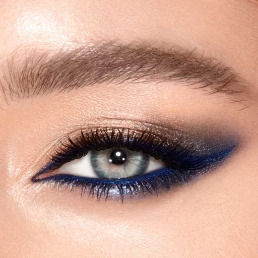 Eye close-up of a model with grey-blue eyes wearing shimmery gold and navy blue eye makeup that makes her eye colour pop. 