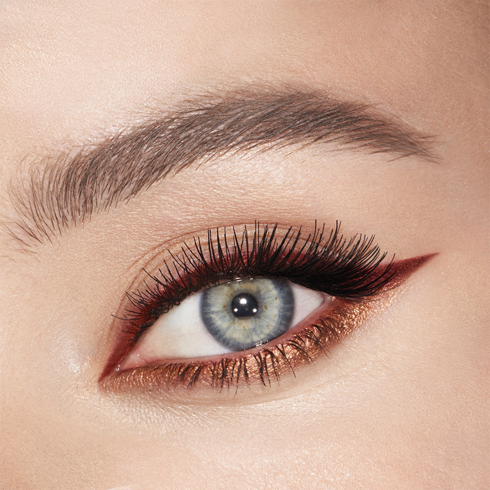 Eye close-up of a fair-tone, blue-eyed model wearing shimmery copper and champagne eyeshadow with a warm-russet and metallic copper eyeliner on the eyelid and lower waterline. 