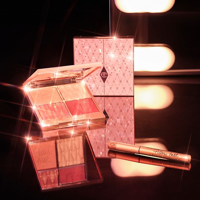 Pillow Talk Crystal Dimension Eyeliner and Pillow Talk Beautifying Palettes displayed An open, face palette with matte and shimmery eyeshadows, blushes and highlighters in shades of pink and gold with a mirrored lid and a vivid pink eyeliner in gold packaging.