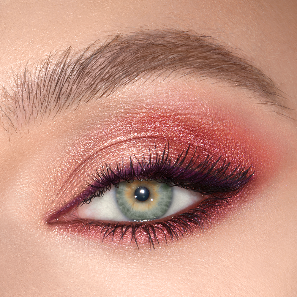 A close-up of a single green eye with shimmery maroon, copper, and gold eye makeup along with plum eyeliner. 