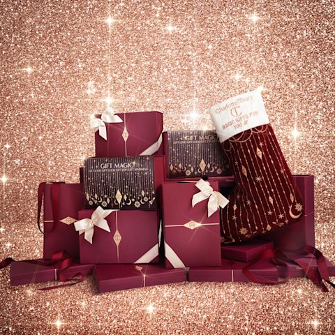 Une grande pile de coffrets cadeaux bordeaux et dorés avec rubans couleur crème noués et bas de Noël décorés.