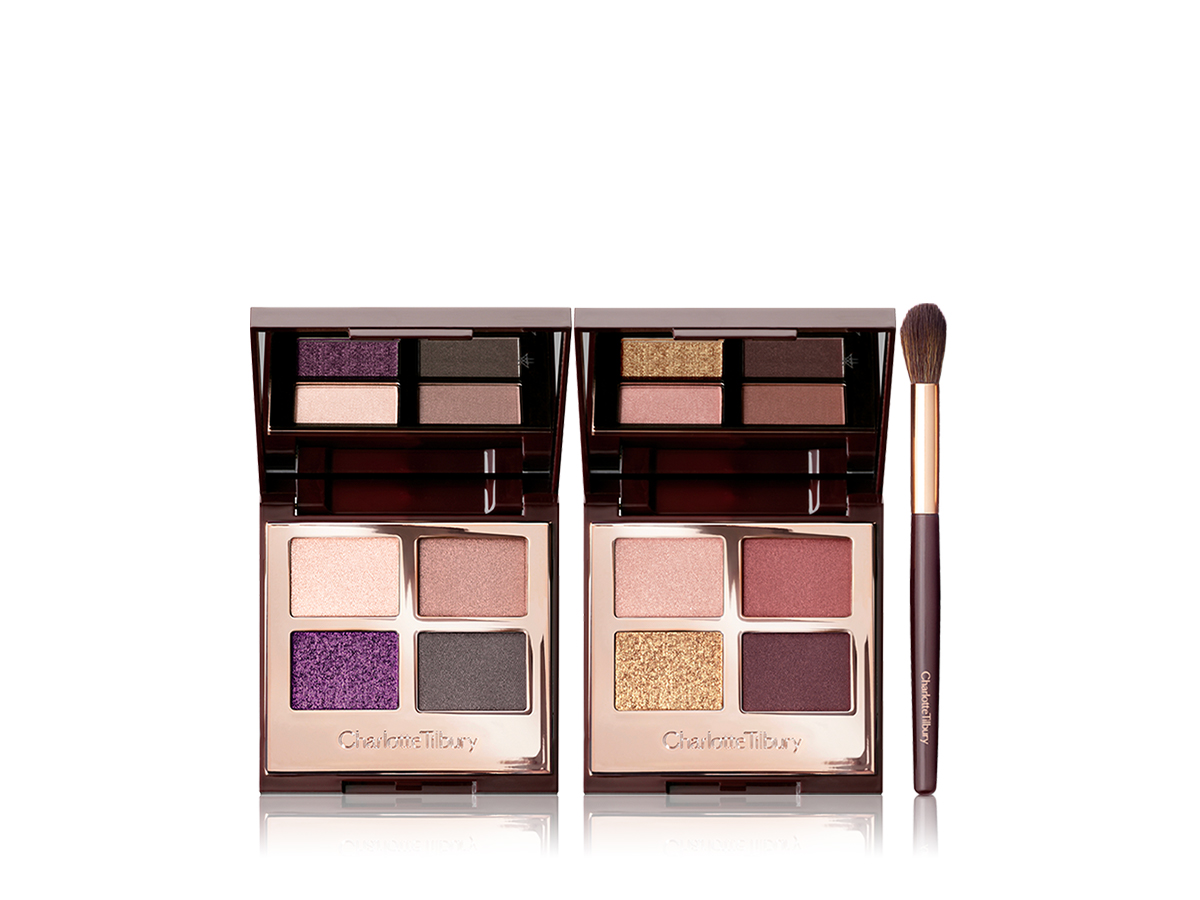 Two, mirrored-lid quad eyeshadow palettes with pink, purple, gold, red, and grey shades along with an eyeshadow blending brush.
