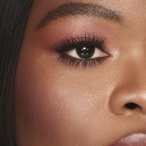 A deep-tone model with brown eyes with a soft and glowy berry-pink blush with gold shimmer.
