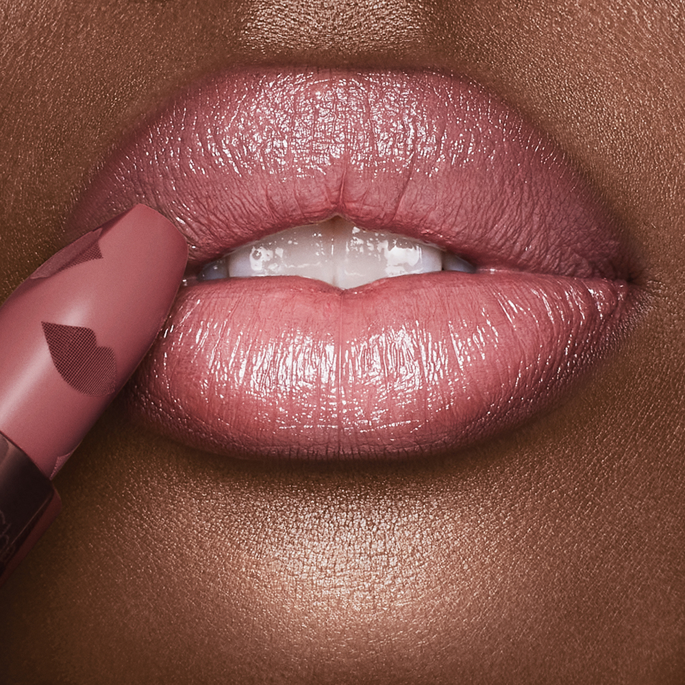 Lips close-up of a deep-tone model applying a muted pink lipstick with a satin finish.