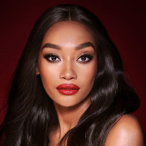 A deep-tone model with brown eyes wearing shimmery bronze eye makeup with muted pink blush and glossy scarlet-red lips