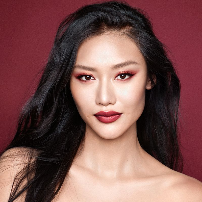 A fair-tone brunette model wearing soft red eye makeup with bold red lips and a glowy face base. 