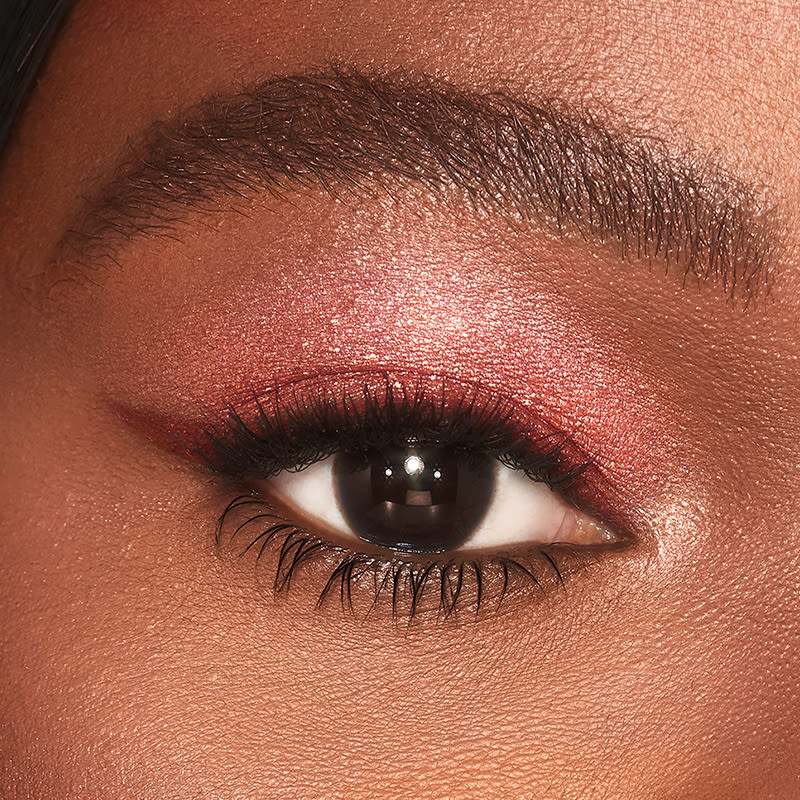 Single-eye close-up of a deep-tone model with brown eyes wearing shimmery berry-pink eyeshadow.