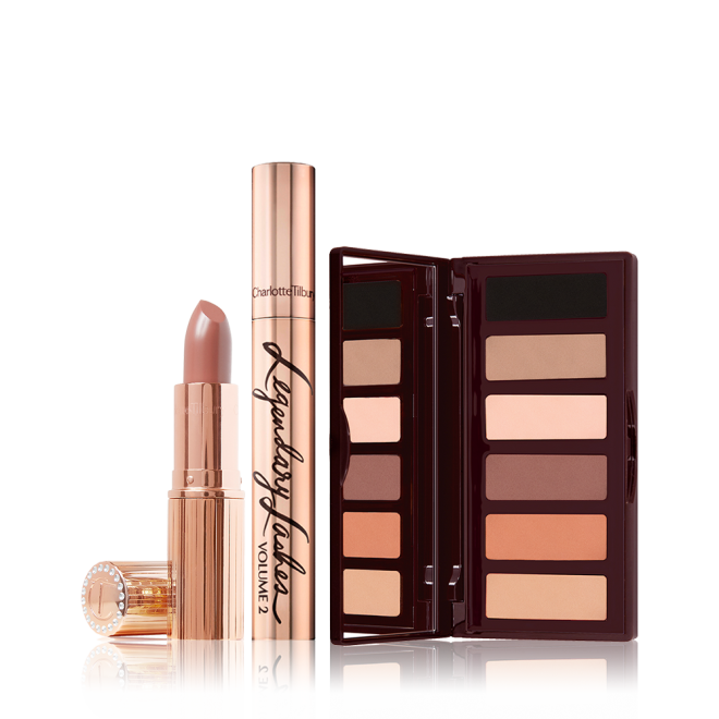 An open cool-beige lipstick with its lid next to it with a closed gold-colour mascara tube, and an open, mirrored-lid eyeshadow palette in nude brown, peach, and beige shades. 