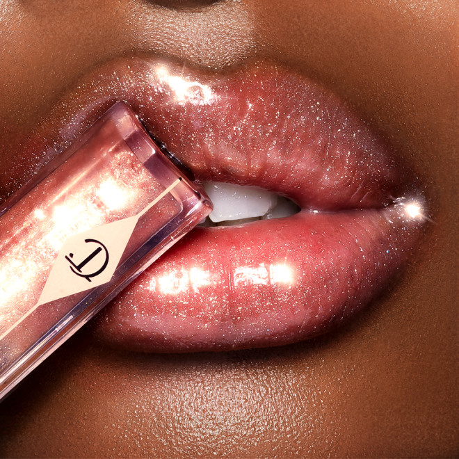 Lips close-up of a deep-tone model wearing a peach-coloured, high-shine lip gloss.