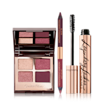 An open, quad eyeshadow with a mirrored lid and eyeshadows in shades of purple and golden with a double-sided eyeliner in shades of maroon, and a black mascara with its applicator next to it. 