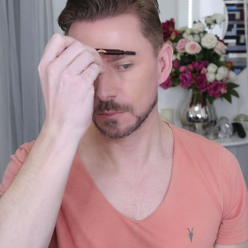 Wayne Goss, a makeup artist, brushing and shaping his brows with an eyebrow brush.