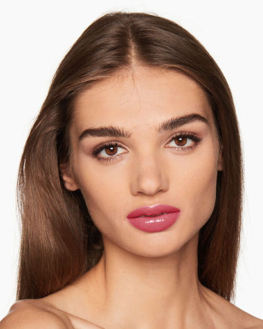 Medium-tone model with brown eyes wearing shimmery champagne eyeshadow with black eyeliner, and high-shine, berry-pink tinted lip oil 